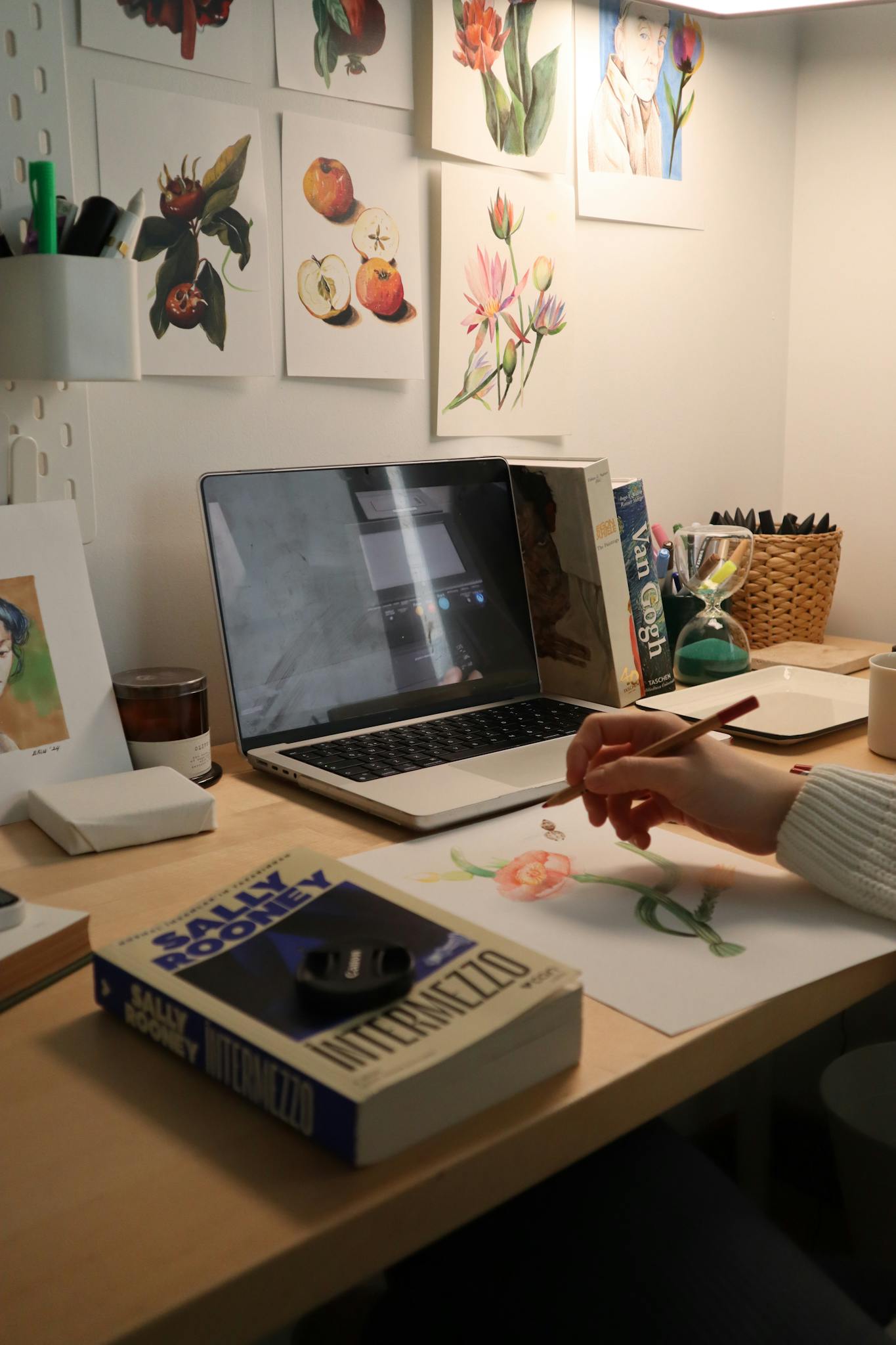 Artist designing watercolor flowers at a creative indoor workspace with books and laptop.