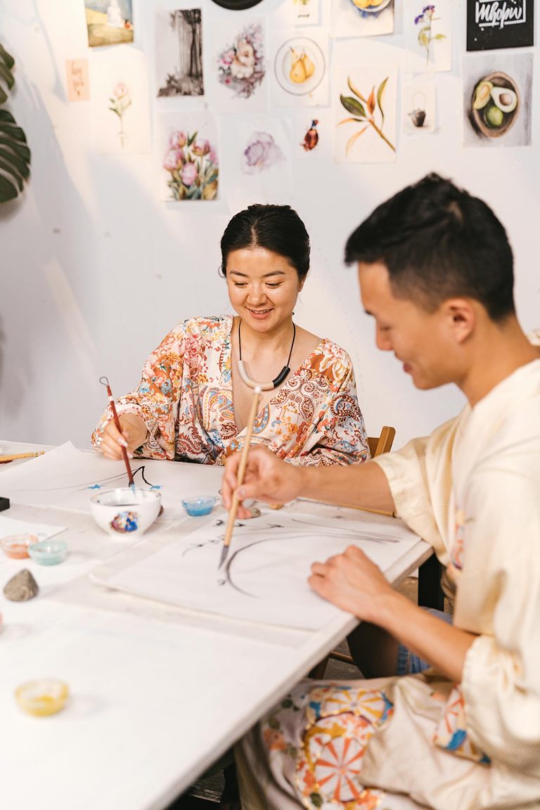 Two adults engaging in a Japanese art class, painting with brushes in a bright studio.